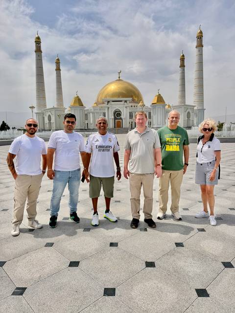       Travelers stand in front of a grand white-and-gold mosque with domes and minarets on a bright day.
  
