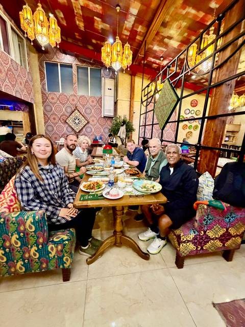       A group of diners enjoy a table full of traditional dishes inside a cozy, colorfully decorated restaurant.
  