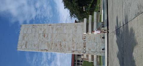       Traveler standing in front of the tall marble Goethals Monument against a partly cloudy sky.
  