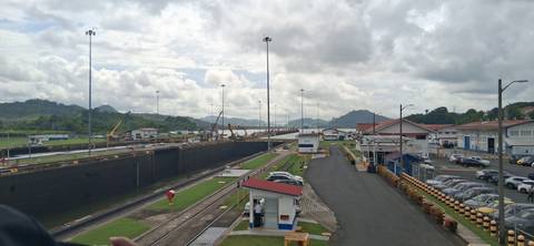       Wide view of Miraflores Locks on the Panama Canal with ships transiting and lush hills beyond.
  