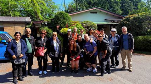       Smiling tour group posing together outside a traditional house on a sunny day
  