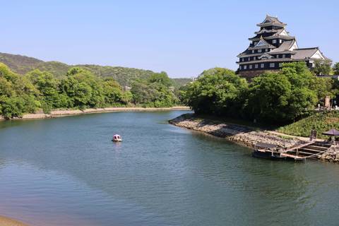       Serene river bend with a small boat and the dark-roofed Okayama Castle on the bank
  
