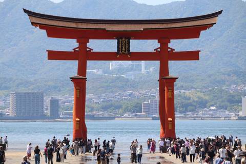       Magnificent red torii gate of Itsukushima Shrine standing in the water with mountains behind
  