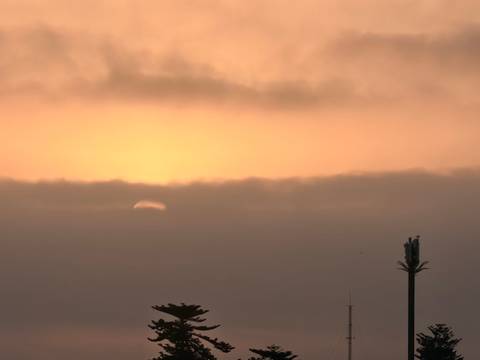       Faint sun sinks into a layer of thick clouds casting an orange glow over a silhouetted antenna mast
  