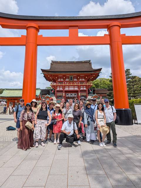       Tour group posing beneath vivid vermilion torii gate at Fushimi Inari Shrine, Kyoto
  