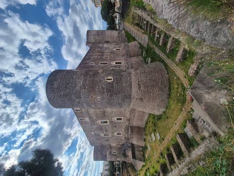       Massive stone towers and walls of Castello Ursino in Catania under a partly cloudy sky.
  