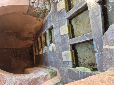       Stone interior of ancient baths with rectangular sunken basins and worn marble slabs.
  