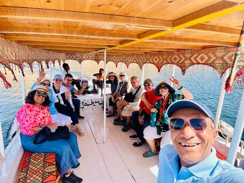       A cheerful tour group waves for a selfie aboard a covered boat on the Nile.
  