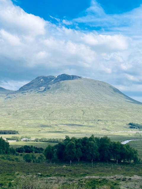       Gentle green mountain slopes under a cloudy blue sky in the Scottish Highlands.
  