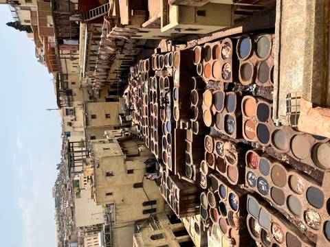       View over rows of circular tanning pits in a traditional Moroccan leather tannery surrounded by yellowed buildings.
  