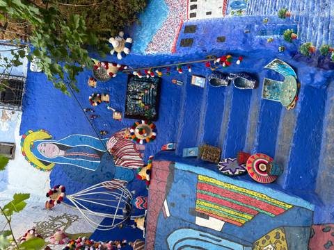       Bright blue-painted staircase in Chefchaouen decorated with folk art, colorful textiles, and handmade crafts.
  