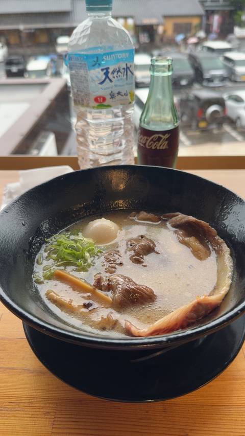       Close-up of a steaming bowl of ramen topped with green onions, soft-boiled egg, and sliced pork.
  