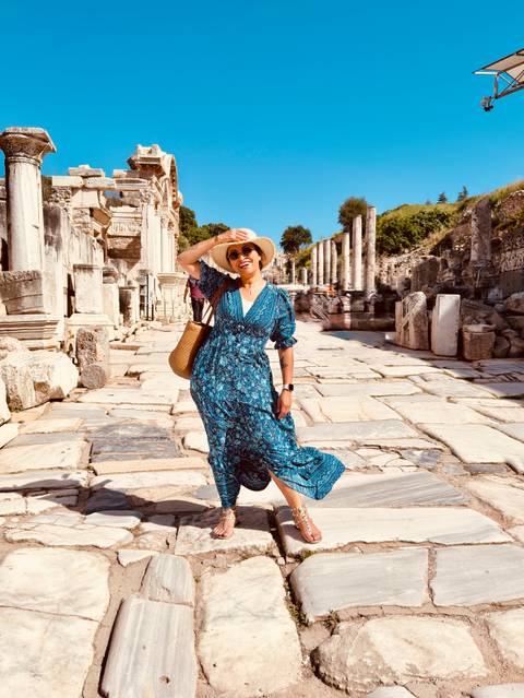       Joyful woman walking along the marble streets of Ephesus surrounded by ancient columns.
  