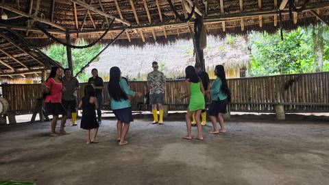       Visitors join local community members in a barefoot traditional dance inside a thatched community hall.
  