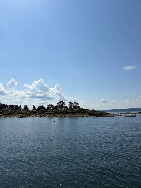       Calm coastal inlet with scattered cottages on rocky islet beneath clear blue sky.
  