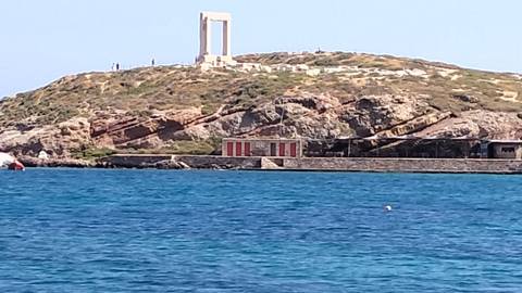       Ancient portal ruin (Portara) atop rocky hill overlooking vivid blue Aegean Sea.
  
