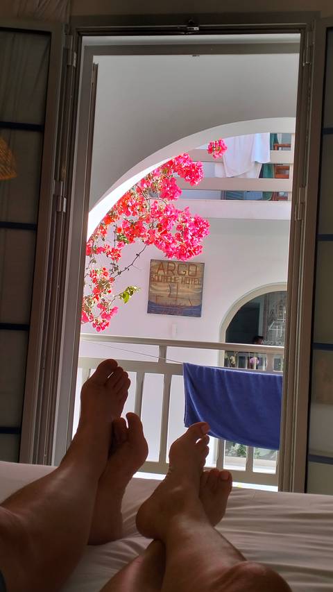       Bougainvillea framing balcony of Argo Boutique Hotel viewed from inside room with relaxed guest’s feet visible.
  