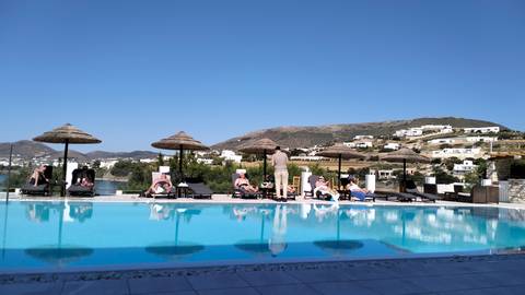       Guests lounging by infinity pool with whitewashed village and hills behind.
  