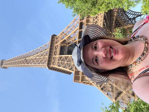       Smiling traveler taking a selfie beneath the Eiffel Tower on a clear blue day.
  