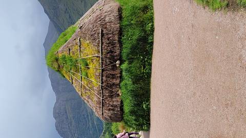       A conical thatched hut covered with grass stands before misty mountains under grey skies.
  