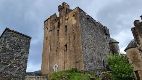       A formidable stone castle rises against a moody sky with rugged walls and turrets.
  