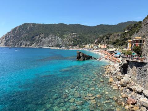       Crystal-clear turquoise water laps against the pebble beach and colorful houses of Monterosso al Mare, Cinque Terre.
  