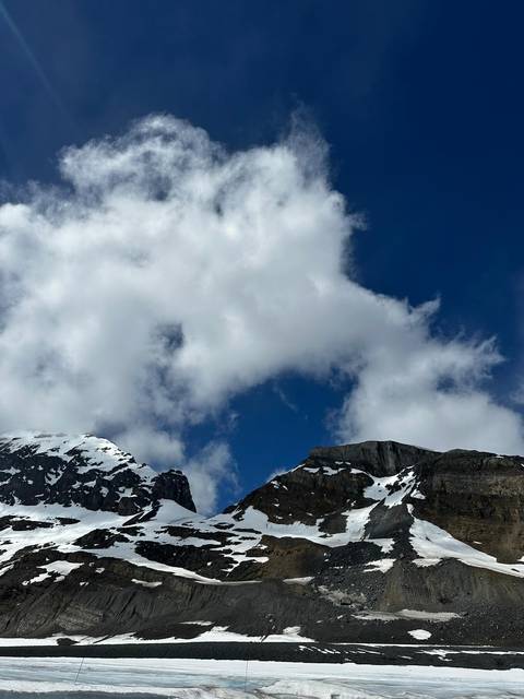       Snow-capped mountain peaks poking through large white clouds against a deep blue Rocky Mountain sky.
  