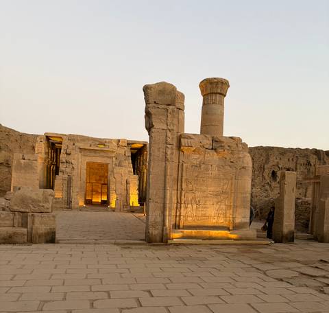       Illuminated sandstone temple entrance at dusk with a lone visitor walking nearby.
  