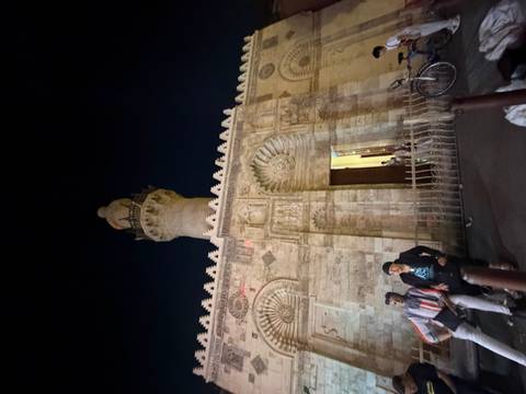       Nighttime street scene with two men sitting near a historic mosque and minaret in Cairo.
  