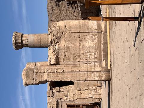       Ancient sandstone pillar and wall reliefs of an Egyptian temple against blue sky.
  