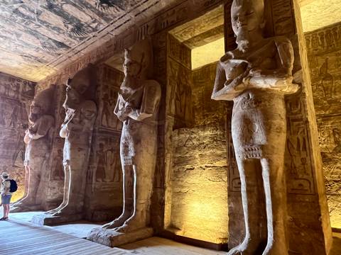       Interior of Abu Simbel temple lined with towering pharaoh statues lit in warm light.
  