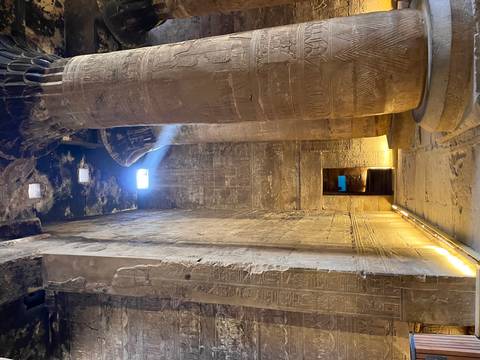       Dimly lit temple corridor with tall carved columns and a beam of light from above.
  