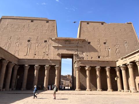       Visitors stand before towering pylons covered in hieroglyphics at an ancient temple.
  