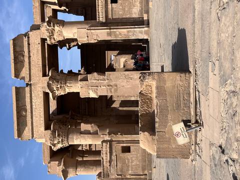       Sandstone columns and carved hieroglyphs form the entrance of an ancient Egyptian temple under bright blue sky.
  