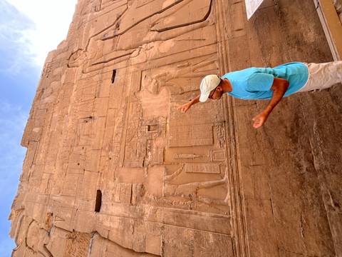       A guide points to detailed wall reliefs on a sandstone temple wall in Egypt.
  