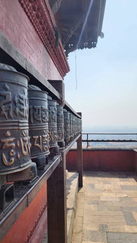       Close-up row of bronze prayer wheels in a Himalayan temple overlooking a hazy valley
  