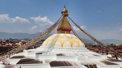       Iconic Boudhanath Stupa draped with prayer flags under a bright blue sky
  