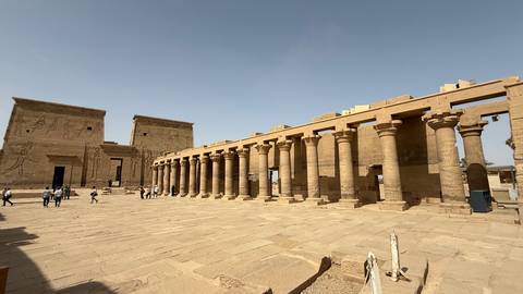       Open courtyard of an ancient Egyptian temple lined with tall stone columns under a clear sky.
  
