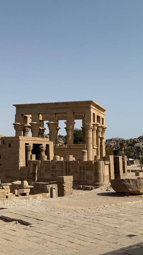       Stone columns and lintels of an ancient riverside temple illuminated by morning sun.
  