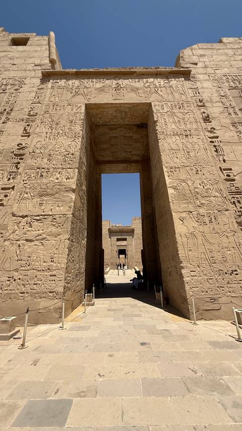       Towering hieroglyph-covered temple gateway framing a deep blue sky.
  