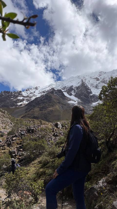       Female trekker gazes at snow-covered Andean peaks and glaciers beneath a bright sky.
  