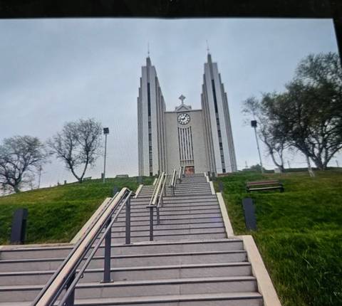       Steep staircase leading up to the modernist Akureyri Church crowned by a clock tower on a grassy hill.
  