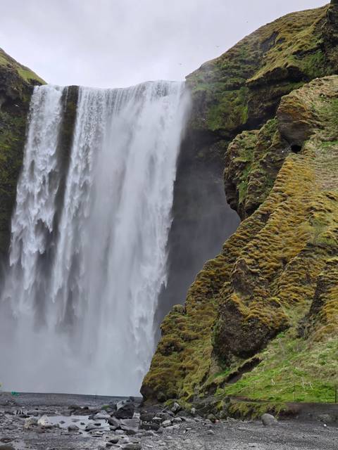       Close-up of the roaring curtain of Skogafoss waterfall beside moss-covered cliff walls.
  