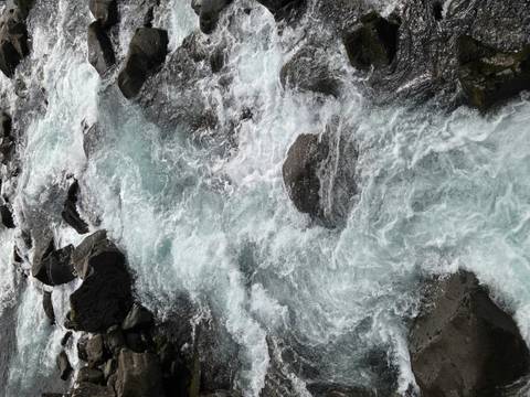       Fast-flowing, foamy turquoise river water rushing over dark volcanic rocks.
  