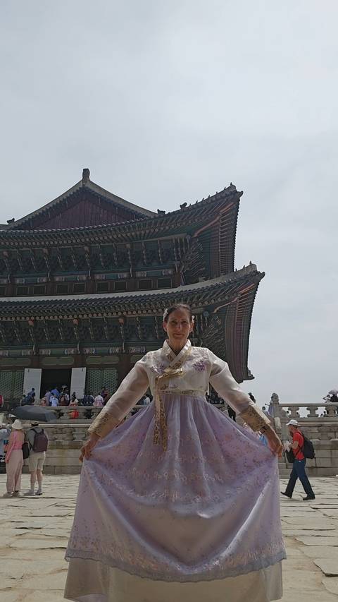       A woman dressed in traditional hanbok stands before an ornate Korean palace building.
  