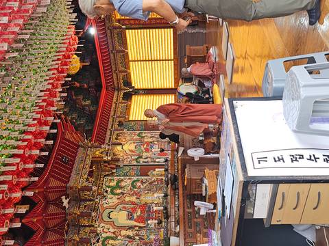       Monks chant inside an ornately decorated temple hall filled with lanterns and Buddhist art.
  