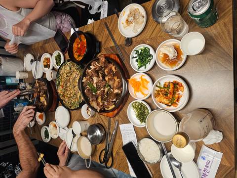       A wooden table is covered with a hearty Korean feast of stews, pancakes and side dishes ready to share.
  