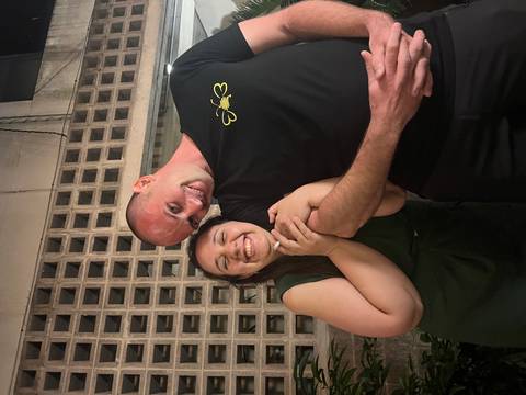       A happy couple embraces and laughs together under soft evening street lighting.
  