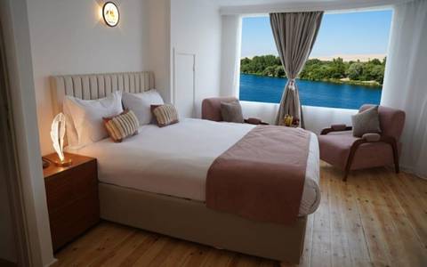       Bright, modern river-view bedroom with large window framing the Nile and desert hills beyond
  