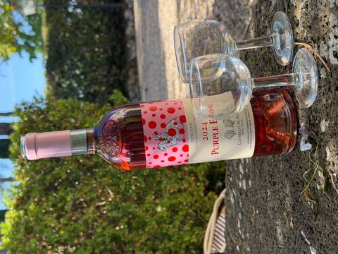       A chilled bottle of Tuscan rosé stands with three empty glasses on a stone table in a garden.
  